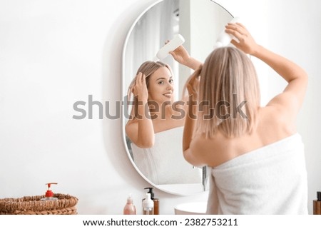 Young blonde woman applying hair product near mirror in bathroom
