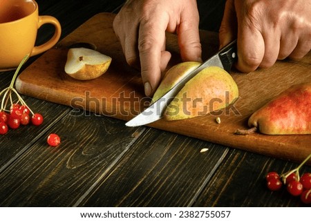 The chef hands use a knife to cut a ripe pear on a cutting board to prepare compote or fruit juice. Pear diet or fruit dessert