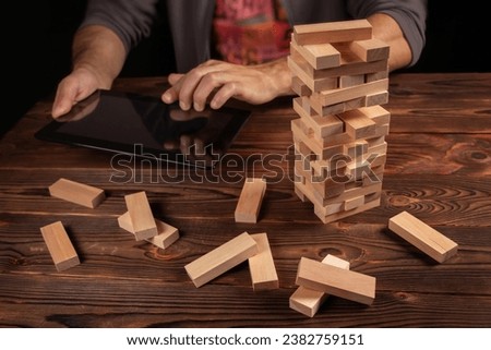 Hand of engineer playing a blocks wood tower game jenga on blueprint or architectural project with tablet. Royalty-Free Stock Photo #2382759151