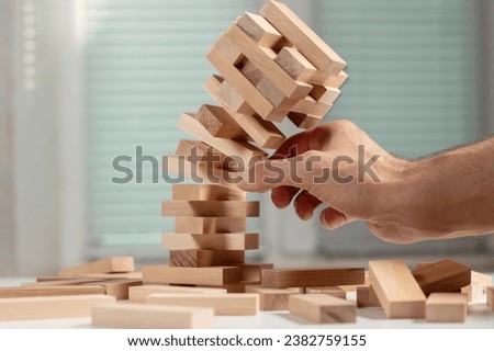 Businessman removing wooden block from falling tower on table. Management of risks and economic instability concept with wooden jenga game. Failure and collapse in corporate business