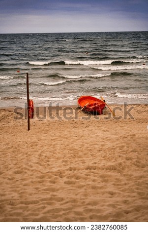 The lifeguard's boat moored on the seashore beach, next to a planted pole on which a lifebuoy is hanging.                               