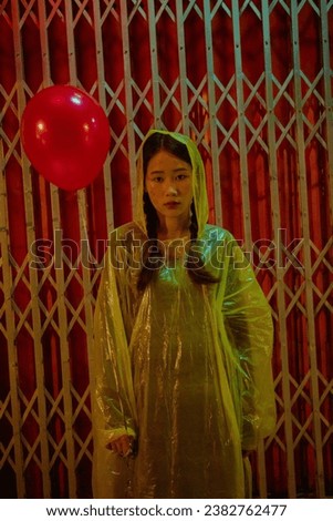 A young woman dressed in a Halloween costume with makeup for the holiday holding yellow balloon and wear a yellow raincoat. 