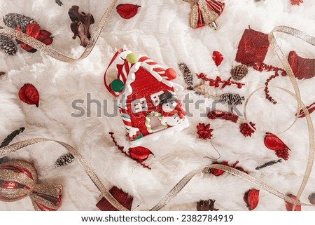 A christmas red house with a snowman on a light background among red Christmas decorations. Christmas bright background with a red house with a snowman and Christmas decorations.