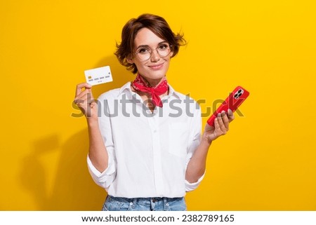 Photo of cute young woman wear shirt red neckerchief hold plastic credit card iphone cashless payment isolated on yellow color background