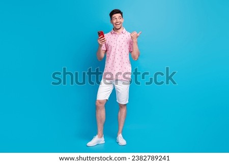 Full body photo of positive guy hold smart phone look indicate finger empty space isolated on blue color background