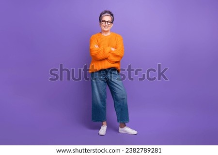 Full length photo of cheerful assertive woman dressed orange sweater denim trousers arms crossed isolated on purple color background