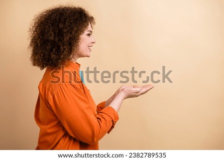 Profile side photo of cheerful gorgeous girl dressed orange trendy clothes presenting empty space isolated on beige color background