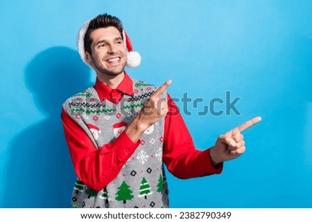 Photo portrait of cute young man look point empty space dressed x-mas print vest hat clothes isolated on blue color background