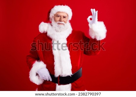 Photo of joyful confident handsome man pensioner dressed santa claus costume showing okey symbol isolated on red color background
