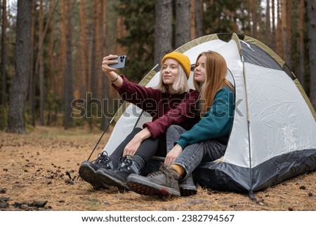 Two young women enjoying the fall forest while sitting in a tent. The concept of spending a weekend in nature.