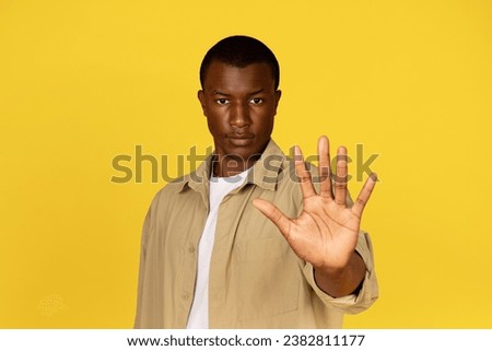 Sad serious strict millennial african american guy in casual making stop sign with hand, isolated on yellow studio background. Human emotions, ad and offer, protest gesture, say no