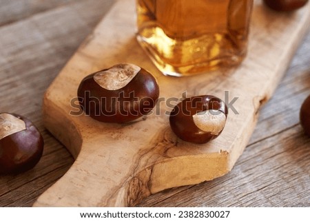 Fresh horse chestnuts on a wooden table with a bottle of tincture in the background