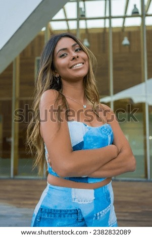 Vertical photo of a pretty woman in denim clothes standing with arm crossed smiling at camera