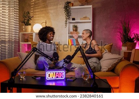 Happy multiracial female radio presenters having a interesting conversation about feminine topics while sitting on a yellow sofa in a cozy studio. Copy space.