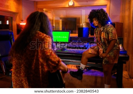 Picture of a talented young female composer sitting on a mixer console in a music studio, listening while her song is being recorded. She is happy, attentively checking the tunes of the recording.