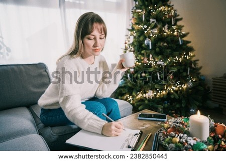Young Woman with cup is hand writing New year's goals on note paper in new year day. New year resolutions list. Goals, resolutions, plans, action, checklist concept. New Year template, copy space Royalty-Free Stock Photo #2382850445