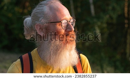 a bearded middle-aged man with glasses in a yellow T-shirt looks at the sunset behind the forest, adventurer, High quality photo