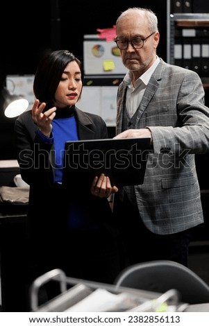 Elderly detective and asian private investigator team checking criminology suspect case file details on laptop. Teamworking investigation coworkers in archival agency depository office Royalty-Free Stock Photo #2382856113