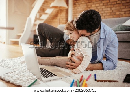 Happy father looking at the laptop with his little daughter at home