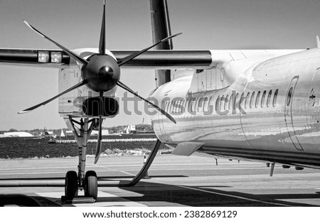 Close-up of black six-bladed propeller and part of wing and fuselage of white modern turboprop airliner in Toronto City Airport with stretch of blue water of Toronto harbor and northern side of