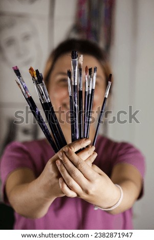 Artistic girl holding many dirty colorful used brushes with both hands.