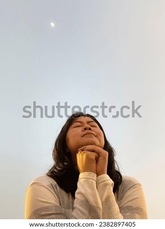 Portrait of beautiful Asian woman folding her hands praying and closing her eyes towards the sky, suitable for design templates and presentation materials
