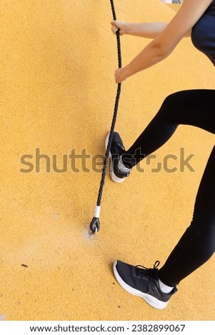 Female hands gripping a climbing rope firmly, with one foot supported on the vertical surface. The yellow background accentuates their determination and bravery as they face the climbing challenge. Royalty-Free Stock Photo #2382899067