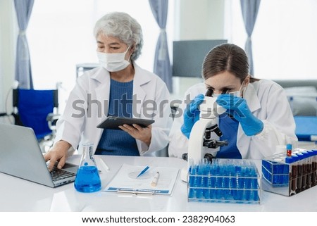 Beautiful young female scientist and two elderly women work in a laboratory with test tubes researching blue chemicals in the healthcare industry.