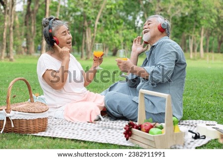 senior couple have a picnic wearing headphone to listen a music and holding orange juice glass in the park
