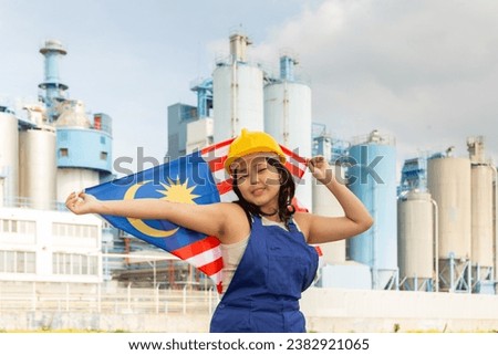 Cheerful asian female worker in hardhat with malaysian flag standing in front of factory