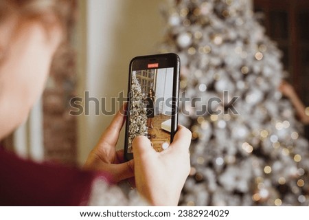take a photo of christmas tree with beautiful Young woman standing near. using smartphone for a picture of bokeh blur Christmas lighting lamp decoration.Happy new year