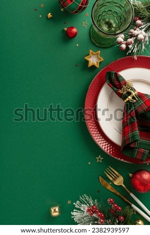 Compose a festive dining table layout. Top view vertical picture of plates, napkin ring, wineglass, ornaments, confetti, frosty fir branches, mistletoe, green background with space for text or ad