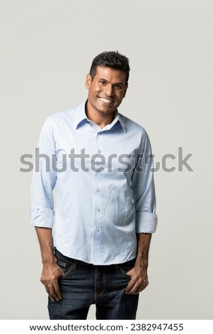 Portrait of a happy Indian man standing in front of a light grey background.  Royalty-Free Stock Photo #2382947455