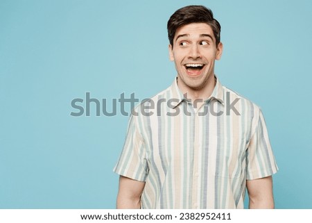 Young surprised shocked excited happy man he wearing striped shirt casual clothes look aside on area copy space isolated on plain pastel light blue cyan background studio portrait. Lifestyle concept