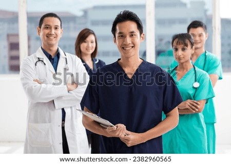 Nurses standing in a hospital with her team in background. Multi-ethnic team of caucasian, Chinese and indian medical staff. Royalty-Free Stock Photo #2382960565