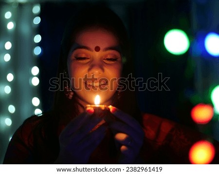 Pretty young female holding an oil-lit lamp in a dark room - festival of Diwali celebration . Smiling Indian woman with a Diwali lamp in hand - an auspicious day, Diwali preparation, bokeh shot Royalty-Free Stock Photo #2382961419
