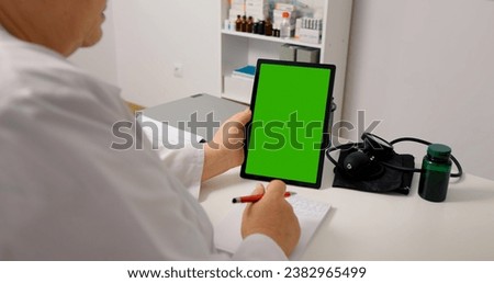 Doctor holds green screen mockup vertical tablet on the desk in office. Telemedicine concept female doctor use green screen tablet pc to see the patient and give advice.