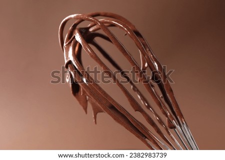 Chocolate cream flowing from whisk on brown background, closeup Royalty-Free Stock Photo #2382983739