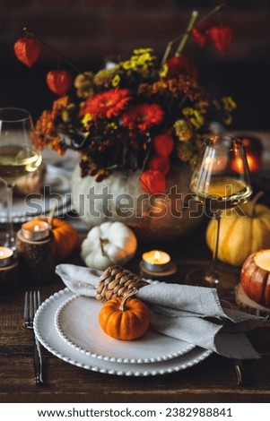 Beautiful elegant table setting for candlelight Thanksgiving Day dinner or Halloween party at home. Fancy dishware, porcelain plates. Floral centrepiece, pumpkins and burning candles as decor