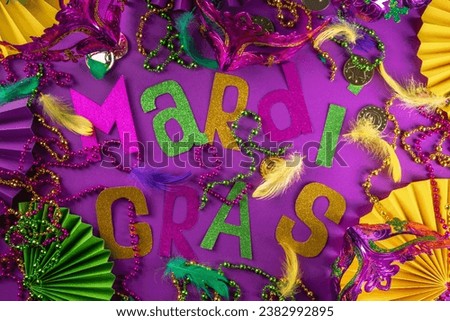 Mardi Gras colorful holiday greeting card background with festival masquerade accessories, decor, carnival mask, beads, feathers, fan on bright background traditional yellow purple green colors