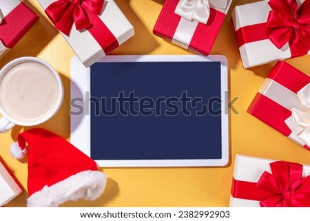 Christmas sale, making wishlist, preparation gifts for Christmas concept. Santa Claus hands with tablet computer, hot chocolate latte cup, gift boxes, flat lay on golden background copy space