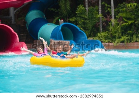 Kids on water slide in outdoor swimming pool. Family in aqua theme park. Children have fun in splash playground. Summer vacation with child. Kid on inflatable tube sliding into a pool. Royalty-Free Stock Photo #2382994351