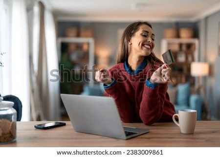 Cheerful female customer looking at credit card and pumping fist after receiving reward for online shopping. Royalty-Free Stock Photo #2383009861