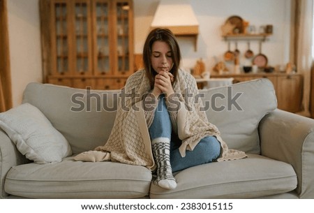 A woman freezes in winter. A young girl in warm woolen socks and wrapped in a blanket tries to keep warm while sitting on the sofa at home. Keep warm. Royalty-Free Stock Photo #2383015115