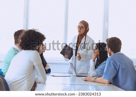 A successful doctor in a hijab confidently presents her work plan to colleagues in a hospital, while using a smart tablet to enhance patient care and communication in the healthcare facility