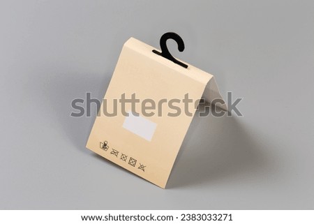 Folding yellow paperboard hanging tag with clothing care symbols on a small plastic hanger on a gray background
