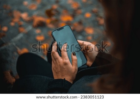 Woman sitting on bench in autumn park using phone , happy mood, fashion style trend. Full frame.