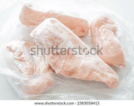 Frozen chicken breast in food plastic wrap or cling film. Photo can be used for how to wrap meat for freezer concept. Royalty-Free Stock Photo #2383058415