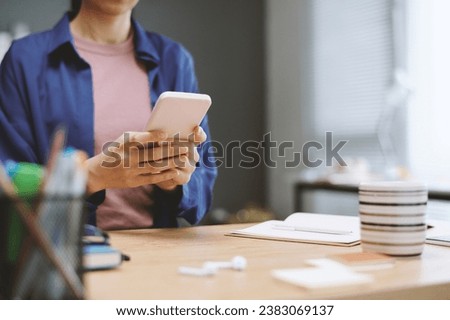 Cropped image of businesswoman checking notifications on smartphone when sitting at office desk