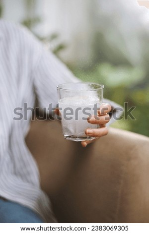 Glass with dissolving fizzy tablet in hand of woman sitting on couch